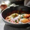 Shakshouka with avocado in a frying pan on a gray table close-up