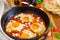 Shakshouka, dish of eggs poached in a sauce of tomatoes, chili, onions in the pan.