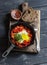 Shakshouka eggs in vintage pan on rustic wooden cutting board on a dark background.