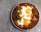 Shakshuka - eggs poached in spicy tomato pepper sauce on a round plate on a dark background