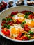 Shakshuka - fried eggs with sausages and vegetables in frying pan