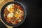 Shakshuka - poached eggs in tomato sauce, onion, pepper and spices in iron pan on dark wooden table with copy space