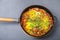 Shakshuka sprinkled with green onions in a frying pan on a gray background.