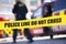 Shallow depth of field image of police tape with action of blurred police officer and emergency vehicles in the background