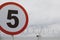 Shallow depth of field selective focus image with a speed limit traffic sign in front of a wall with razor wire on top, outside