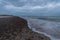 Shallow foamy waves washing the sand of a rocky beach under a cloudy sky in Denmark