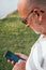 Shallow focus of an elder Caucasian man looking through his mobile phone while at a park