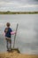 Shallow focus of a kid with a wooden stick for fishing standing near the lake under a cloudy sky