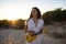 Shallow focus shot of a female in a white dress posing at the beach while holding a yellow ukulele