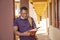 Shallow focus of a young African male with a facemask reading a book at a campus area