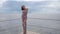 Shapely feminine body to embankment, slender girl in bathing suit on coast sea, happy woman standing on jetty