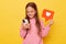 Sharing popular content on social media. Smiling little girl wearing pink sweatshirt holding blogger heart like icon and using