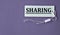 SHARING - word on white paper with thread on a purple background
