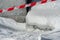 Sharp and dangerous icicles falling from the roof. Close-up of the protective white and red ribbon on the background of snow and