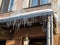 Sharp icicles a lot and melted snow hanging from eaves of roof and downpipe. Frosty sunny day