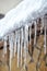 Sharp icicles and melted snow hanging from eaves of roof. Beautiful transparent icicles