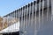 Sharp icicles and melted snow hanging from the eaves of the roof. Beautiful transparent icicles slowly gliding of a roof