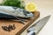 Sharp kitchen knife and two raw mackerels, black peppercorns, dill and lemon on a brown wooden cutting board. Seafood, healthy