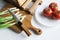 Sharp knife, green onions, vintage solid oak wooden cutting boards and fresh tomatoes in a plate on a light background. Preparing