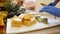 Sharp knife in human hands in rubber blue gloves cuts cheese into pieces on white tray close-up