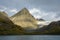 Sharp mountain peak highlighted by the sun against a stormy sky, glacier, grassy hills rising up from ocean and beach, Coopers Bay