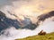 Sharp snowy peaks of Alps mountains above valley full of heavy fog, end of summer