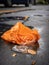A sharp tear in an orange trash bag spilling its contents out onto the pavement.. AI generation