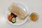 Shaurma or doner on a white plate, next to a piece of cucumber and tomato with mayonnaise and ketchup. Fast food. A glass of lemon