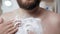 Shaving male chest concept. Bearded caucasian man in bathroom is applying shaving foam to his hairy chest. Close-up