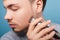 Daily shaving routine. Closeup portrait of young man grooming cheek with closed eyes. isolated on blue background