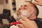 Shaving with straight razor in a barbershop. A bearded old man being shaved in a barbershop. Classic shave by Stainless Steel