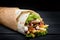 Shawarma rolled in lavash, moist grilled meat with onion, herbs and vegetables on wooden black background.