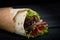 Shawarma rolled in lavash, moist grilled meat with onion, herbs and vegetables on wooden black background.