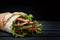 Shawarma rolled in lavash, moist grilled meat with onion, herbs and vegetables on wooden black background.