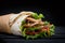 Shawarma rolled in lavash, moist grilled meat with onion, herbs and vegetables on wooden black background.