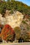 Sheer rock bluff in the Autumn with pinen trees growing on top and trees with colored foliage and a two lane highway and mailbox b