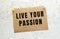 A sheet of craft paper with LIVE YOUR PASSION text attached to a white textured wall with a button. Office reminder.