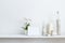 Shelf against white wall with decorative candle, glass and rocks. Potted orchid plant