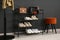 Shelving rack with shoes and accessories near black wall at home. Idea for hallway interior design