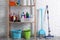 Shelving unit with detergents, cleaning tools and toilet paper near white brick wall