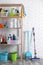 Shelving unit with detergents, cleaning tools and toilet paper near white wall indoors