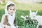 A shepherd girl in a white dress and bonnet feeds a goat with cabbage leaves