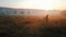 A shepherd leads a herd of goats to pasture. Early morning, golden sunlight. In the background is a field and mills