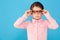 Shes seriously smart. A serious little girl holding the sides of the spectacles against a blue background.