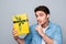 Shhh! Look what I have but keep silence. Portrait of funny, attractive man holding forefinger on lips, showing gift in yellow pac