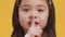 Shhh, it\'s secret. Close up of little girl putting finger on lips, showing silence gesture, orange studio background