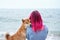 A Shiba Inu dog cozily nestles into a woman with striking pink hair
