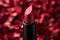 Shimmering red lipstick over blurred background. Metallic and glossy lip stick tube on burgundy backdrop. Makeup beauty
