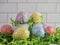 Shimmery Easter Eggs in purple, yellow, pink and blue with little white metal buckets on top of green paper shreds with a white