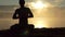 Shining man sits on a lake bank, prays and practices yoga at sunset in slow motion.